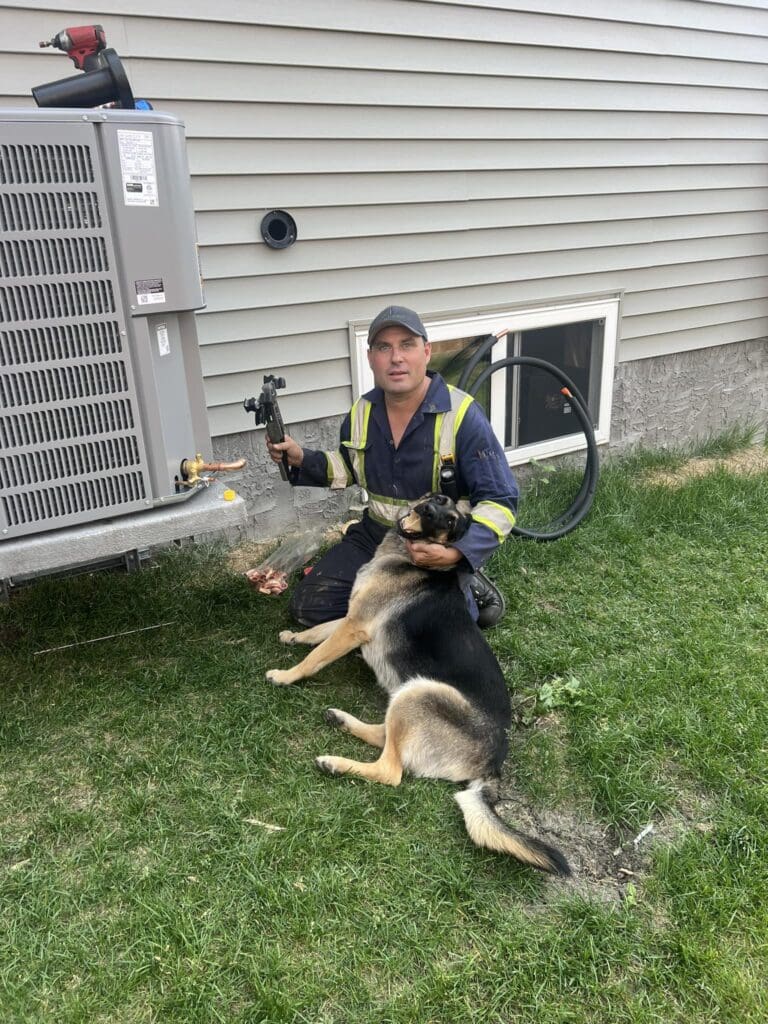 AC replacement in ST Albert, Jaxon owner of Heartland by an AC with a tool on his right hand and petting the clients dog with his left