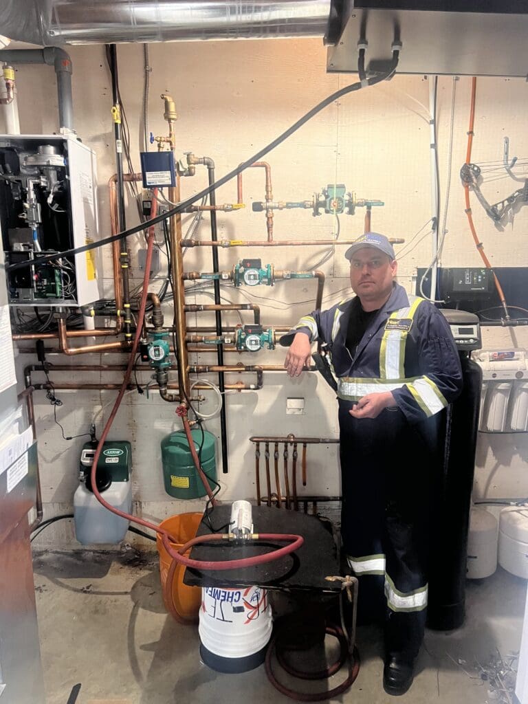 Jaxon owner of Heartland plumbing and Heating Ltd, beside a boiler and hydronics installation